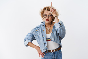 Girl looking with dismay at losers. Portrait of arrogant and confident good-looking stylish woman with short blond haircut mocking rival showing L letter on forehead and grimacing like snob