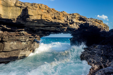 Lava rock arch over the ocean with waves passing splashing underneath, Poipu, Kauai
