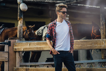 Young attractive bearded man wearing a white empty t-shirt without logo and black jeans is standing on a western town background. Horizontal mock up style.