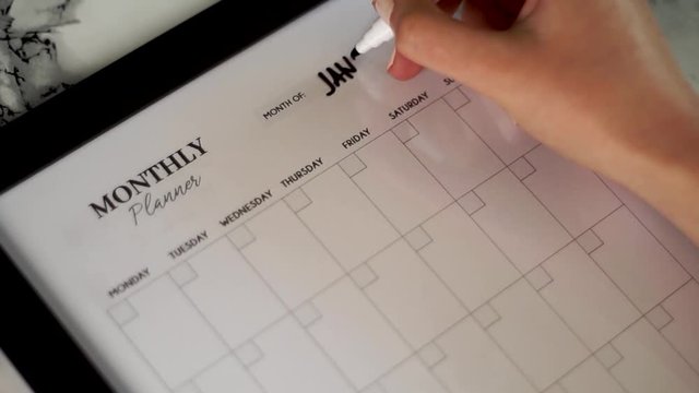 Female hand writing January on her monthly planner calendar, close up