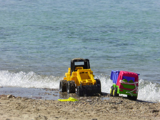 Colorful plastic truck and bulldozer childrens toys, abandoned at a sandy beach ready to be washed into the sea by the first incoming waves of the tide.