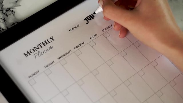 Female hand writing June on her monthly planner calendar, close up