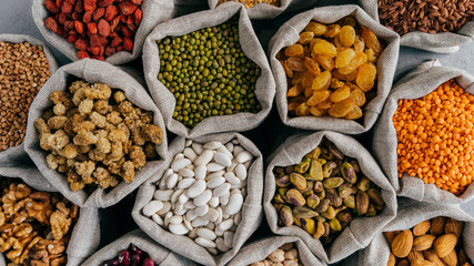 Healthy cereals and dried fruit. Close up top view of small bags with dry legumes seeds. Different types of beans. Natural grains.