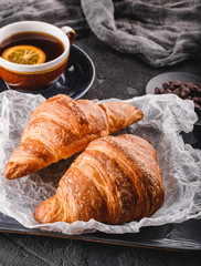 Breakfast with fresh french chocolate croissants on paper over dark background with napkin and cup of tea. Dessert, puff pastries, closeup