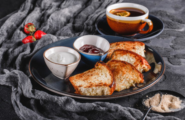 Breakfast with sweet homemade buns on plate over dark background, yogurt, strawberry jam, a cup of tea. Bakery, pastry, dessert, closeup