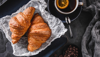 Breakfast with fresh french chocolate croissants on paper over dark background with napkin and cup of tea. Dessert, puff pastries, top view