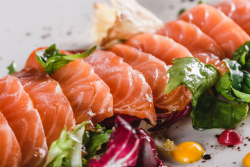 Salad of sliced salmon fillet with lettuce, cabbage and sauce in plate on dark grey background. Healthy food, clean eating, dieting, closeup