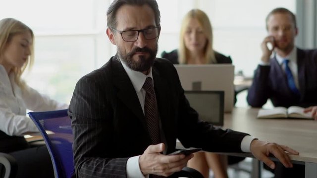 Leader of business team is cheking his mobile and smiles to camera