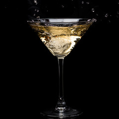 in a martini glass, vermouth ice falls, and splashes with drops on a black background