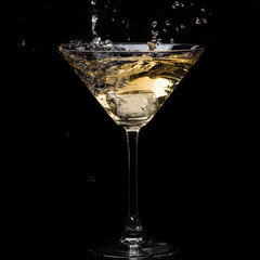 in a martini glass, vermouth ice falls, and splashes with drops on a black background
