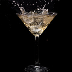 in a martini glass, vermouth ice falls, and splashes with drops on a black background