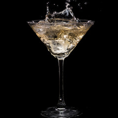 in a martini glass, vermouth ice falls, and splashes with drops on a black background