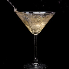 in a martini glass, vermouth ice falls, and splashes with drops on a black background