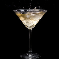 in a martini glass, vermouth ice falls, and splashes with drops on a black background