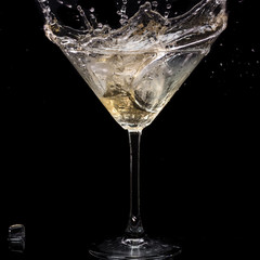 in a martini glass, vermouth ice falls, and splashes with drops on a black background