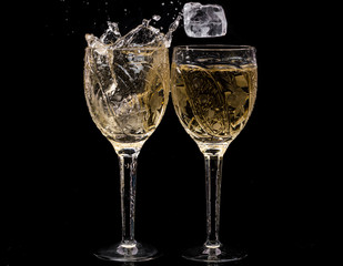 Two crystal wine glasses with a drink, falling ice and splashes