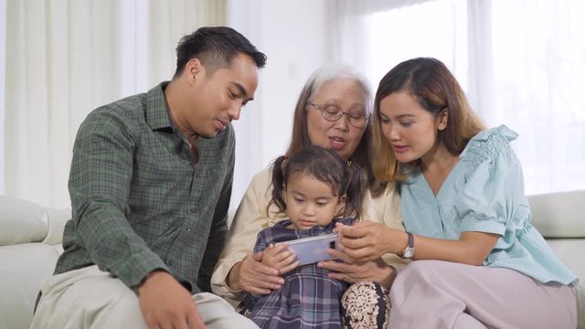 Cute little girl using a mobile phone with her parents and grandmother on the sofa at home. Shot in 4k resolution