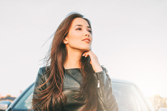 Beautiful charming brunette long hair young asian woman in black leather jacket near her car