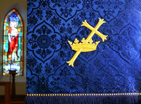 Close up of blue church parament with stained glass good shepherd window. Concept that Christ is King and will return.