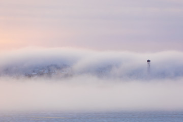 Thick fog at sunrise over hill and city buildings