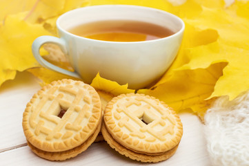 Cup of tea with cookies on white table with autumn leaves and warm scarf.