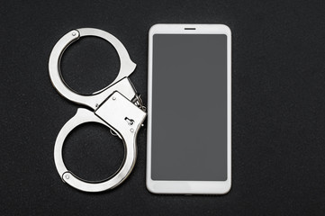 Smartphone with handcuffs on black background. Top view.