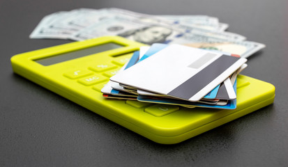 Stack of credit cards with calculator and money on black.