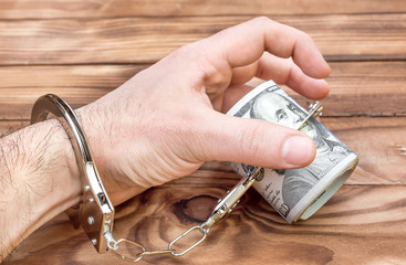 Man's hand in handcuffs taking money on the table.