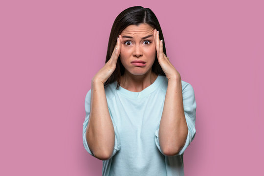 Isolated facial expression of a worried, concerned, fearful, regretful woman, expressing distress and inner conflict, pink background