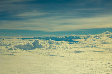 dark blue silhouettes of himalayan mountains stick out of white clouds under blue sky aerial view