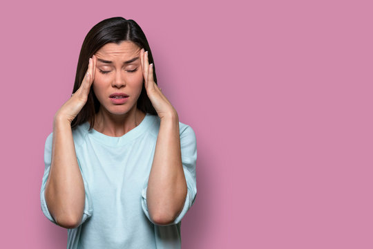 Woman overwhelmed with stress and concern, confusion and doubt, hands to head, on pink background copy space