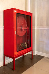 Red Fire Hose Cabinet on brown tile floor against white wall.