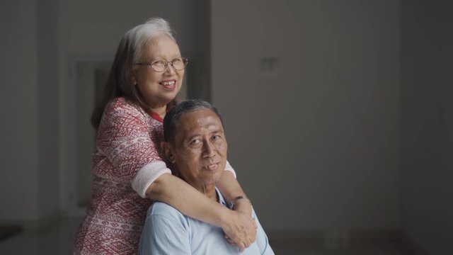 Slow motion of happy senior couple smiling at the camera with the man recovering from stroke disease and sitting on wheelchair