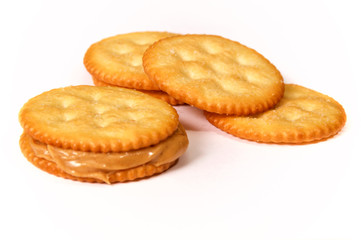 Natural organic peanut butter fills and oozes out of this sandwich made with golden round crackers on white background with other crackers