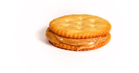 Side view of Natural organic peanut butter filling and oozing out of this sandwich made with golden round crackers on white background.