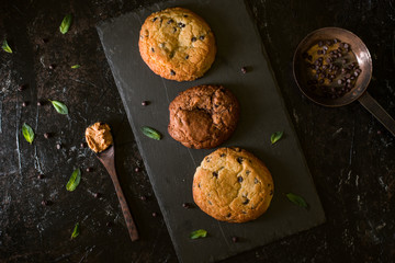Top view of a handcrafted chocolate cookies with chocolate chips on dark surface with milk pitcher on backdrop.