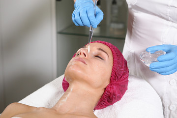 A cosmetologist puts a remedy on the face for the patient to nourish, moisturize and rejuvenate the skin. Cosmetic procedure in the clinic. Close-up of the patient's face. Beautician office