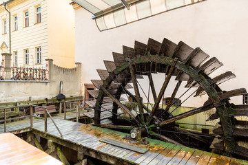 Side view of an old ancient wet wooden waterwheel with surrounding city buildings and architecture in Prague.