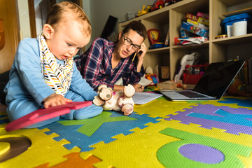 Mother working on her computer while taking care of her baby at home, multitasking woman, concept...