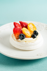 Pavlov's meringue cake with cream and glazed fruit on turquoise tablecloth