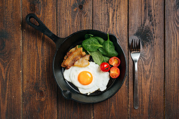 Top view of tasty bacon, egg, spinach and tomatoes with fry pan on the wooden table.