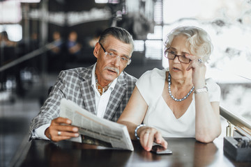 Two beautiful seniors couple waiting their coffe at summer terrace ,and reading newspaper at this time