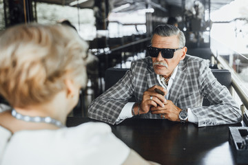 Stylish senior man sitting in summer terrase with woman,and discution about work.Lifestyle,beautiful day