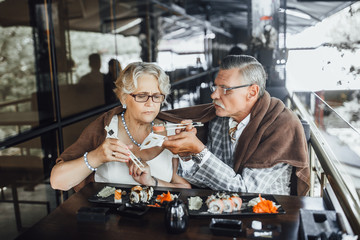 Fototapeta na wymiar Content couple seniors man and woman sitting at summer terrace eating sushi and spending time together happily,family