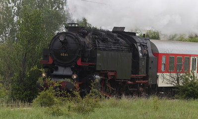 Fototapeta na wymiar Historic steam locomotive with passenger wagons speeding on railroad tracks curve and blowing heavy white smoke near Sofia