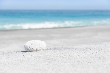 Fototapeta na wymiar Stone on the beach before aqua colored sea in summer.