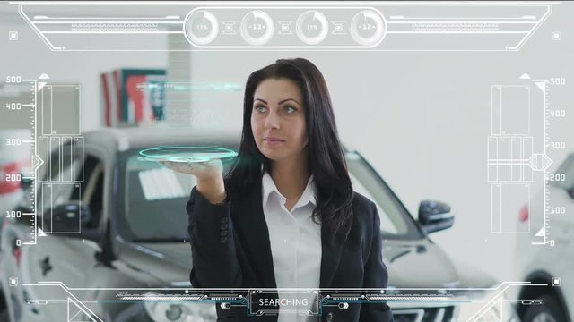 Fashionable girl in black jacket standing in the auto show holds a tablet and shows the animation of the SELF DRIVING