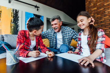 Family concept. Two grandchildren paint with grandfather on living room.
