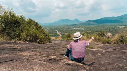 Fototapeta na wymiar Senior asian traveller pointing towards faraway from top of a mountain in Sri Lanka