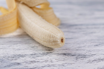 Peeled half banana on light wooden background